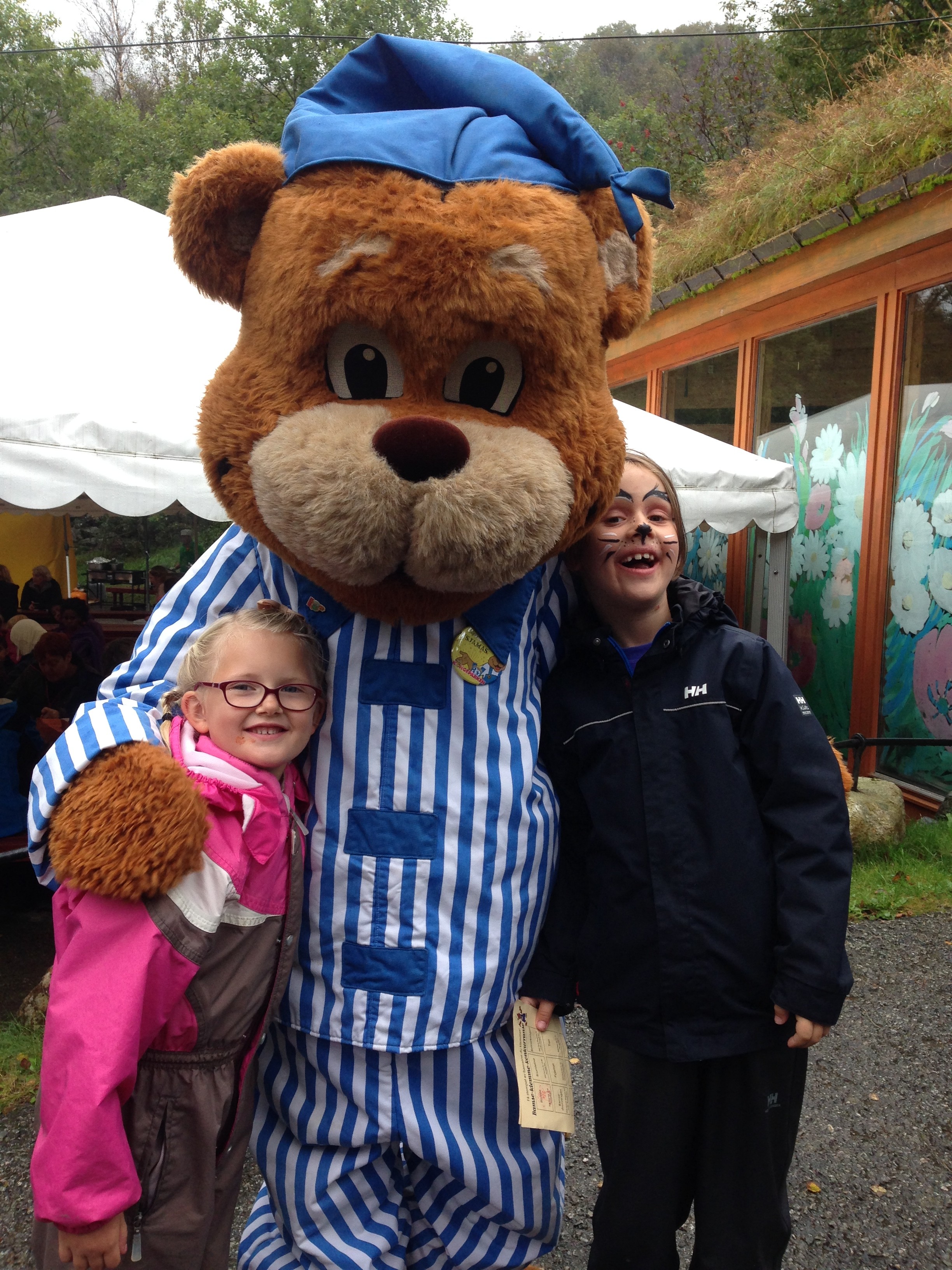 Kongeparken-maskoten Bamse holder rundt to barn som smiler. 